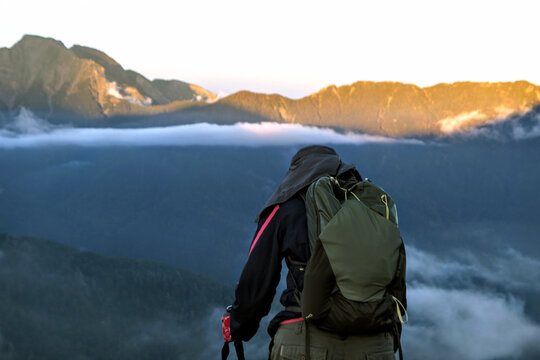 View of a hiker with a backpack standing before mountain ranges with mist and golden light in Switzerland.
