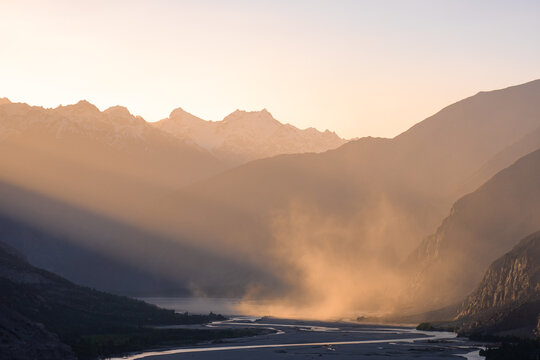View of the khaplu mountain range at golden hour with a winding river and dust particles illuminated by soft sunlight in Khaplu, Gilgit, Pakistan.