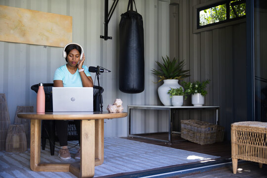 African American woman sitting in studio wearing headset recording podcast with laptop and mic
