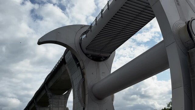 Low angle view of the Falkirk Wheel rotating boat lift against a cloudy blue sky, massive modern steel waterway infrastructure and engineering marvel in Scotland.
