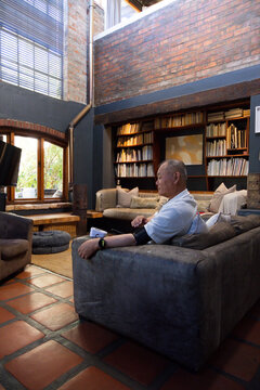 Senior Asian man sitting on gray suede sofa in living room, using blood-pressure cuff, copy space
