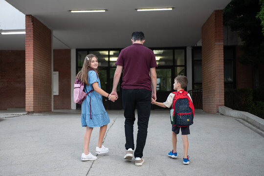 Back to school and education concept, father walking children to school holding hands with backpacks, family support and parental guidance for students.