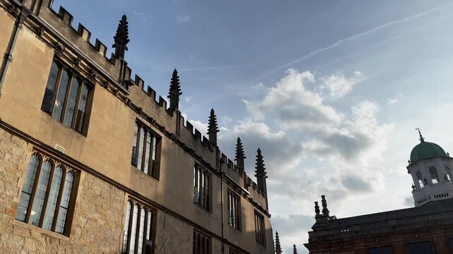 Beautiful historic stone architecture, classical facades, and spires of Oxford University campus buildings under blue sky, England.