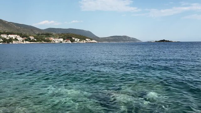 Peaceful mediterranean coastal landscape with clear blue adriatic sea, rocky shoreline and distant seaside village.