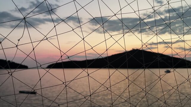 Blurred sea and island landscape at dusk viewed through a focused nautical fishing net, maritime concept.