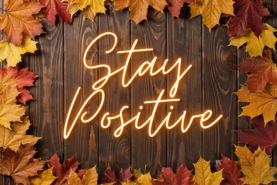 Stay positive neon sign on a rustic wooden background framed with colorful autumn leaves