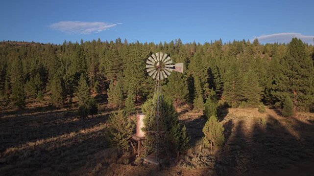 Aerial drone flyby of ranch windmill and storage tank at Dow Wells, bathed in warm evening light, Lassen County, Northern California.