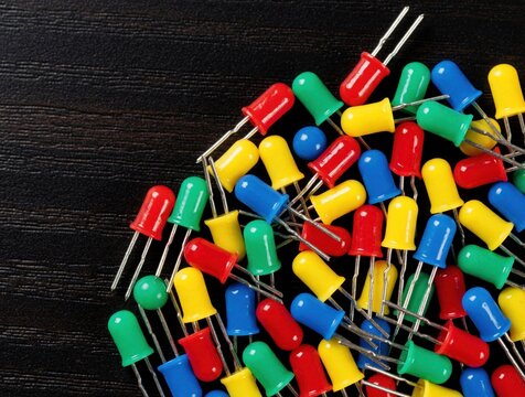 Scattered colorful light emitting diodes on dark surface. Electronic components in red, blue, green, and yellow are used for tech projects and DIY circuits. Macro view.