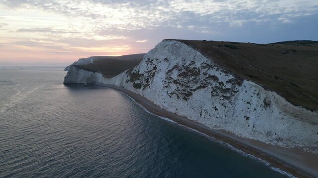 Drone flying left and away from dramatic white chalk cliffs at sunset