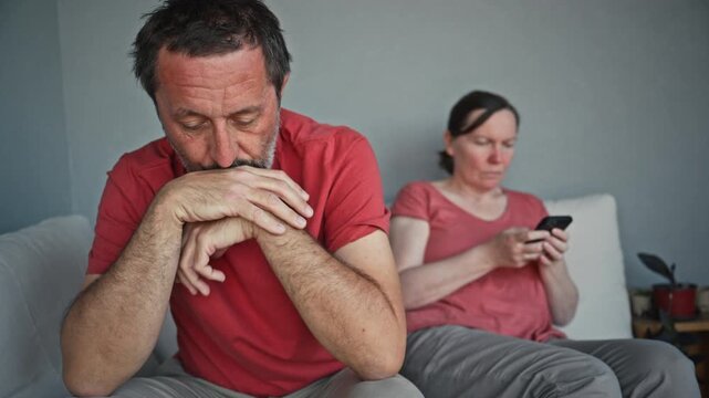 Distant couple sitting on sofa during relationship strain while woman focuses on phone, 4K
