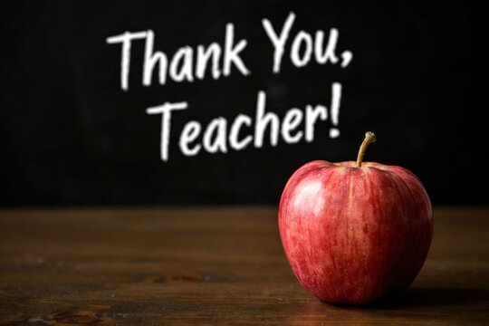 Red apple on a wooden desk with a chalkboard background saying thank you teacher