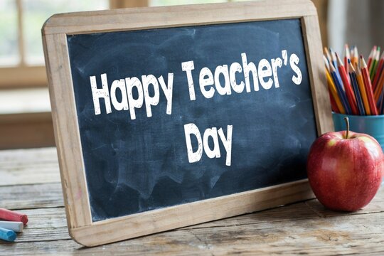Happy teachers day message written on a chalkboard with an apple and pencils