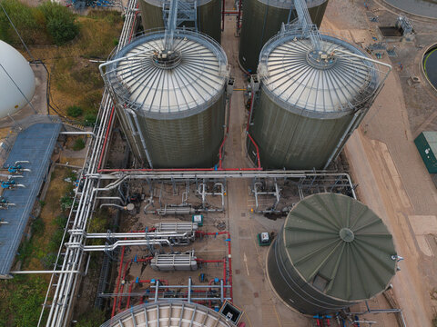 Aerial view of the wastewater treatment plant featuring large industrial storage tanks, complex piping systems, and infrastructure in Wanlip, England, United Kingdom.