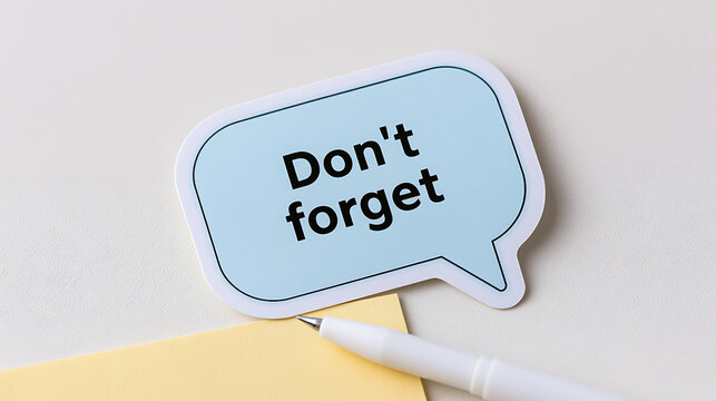 Adhesive sticky note featuring the text don forget in a speech bubble shape next to a white pen on a clean neutral desk surface area