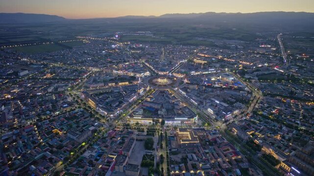 High-Angle Aerial Panoramic View of Tekes Bagua City Nightscape at Dusk, Ili Unique Bagua I-Ching Geometric Layout, City Lights, Radial Streets, Mountain Range and Horizon in Xinjiang