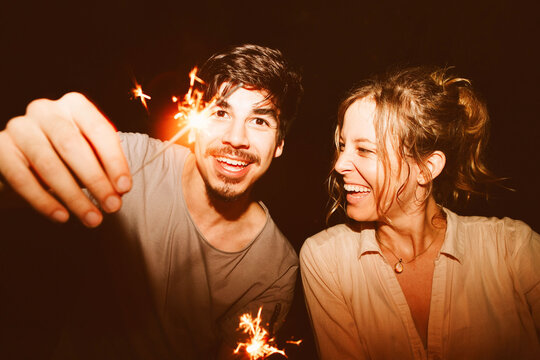 Happy couple laughing with sparklers at a night celebration