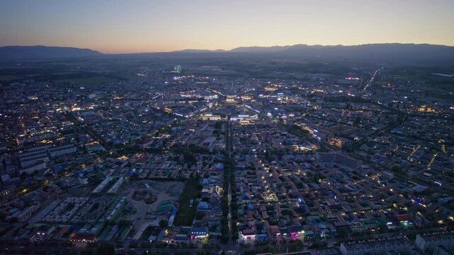 High-Angle Aerial Panoramic View of Tekes Bagua City Nightscape at Dusk, Ili Unique Bagua I-Ching Geometric Layout, City Lights, Radial Streets, Mountain Range and Horizon in Xinjiang