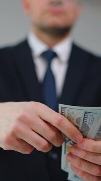 Formally dressed man carelessly throws US Dollar bills towards the camera