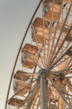 Large amusement park Ferris wheel silhouetted against a calm blue summer sky, featuring vintage-style passenger cabins and detailed steel framework.