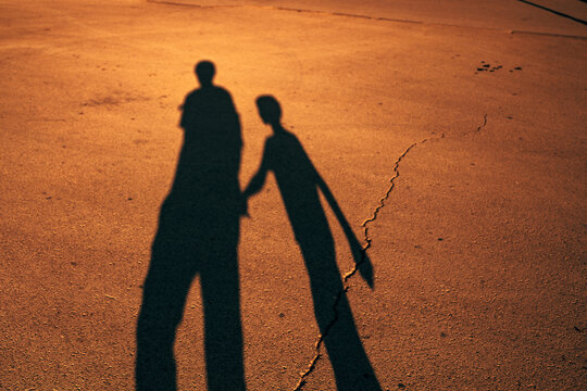 Silhouettes and shadows of parent and child walking together at golden hour. Concept of family bonding, guidance, love, trust, and parenting.