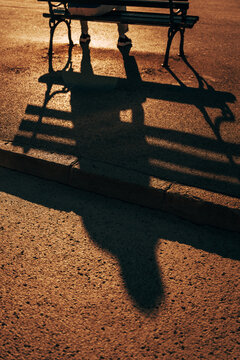 Silhouette and long shadow of a person seated on a park bench at sunset. Concept of solitude, quiet moments, relaxation, and urban life.