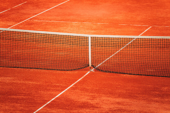 Empty red clay tennis court with black net in soft daylight. Concept of sports competition, outdoor training, fitness, and active lifestyle.