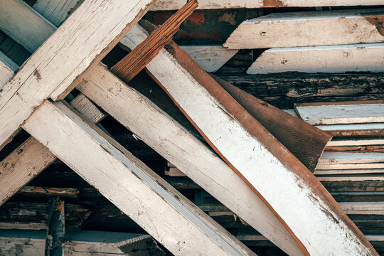 Full frame background of weathered wooden planks with peeling white paint crisscrossing in a construction scrap pile.