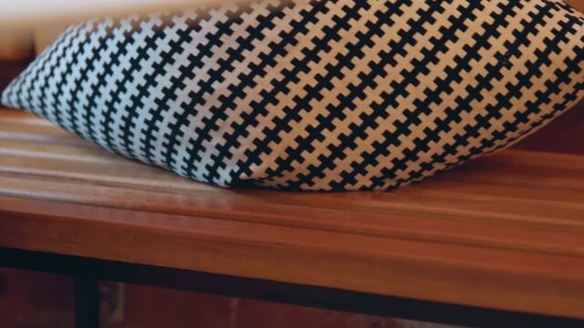 Close up of black and white houndstooth patterned pillow resting on wooden bench with brick wall background. Person wearing blue jeans sits next to pillow partially visible in some frames