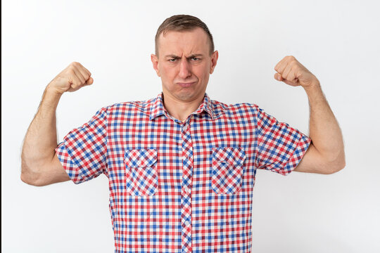 Man in a plaid shirt flexing his biceps with a humorous, pouting expression, pretending to be strong while looking mockingly weak against a clean white studio background