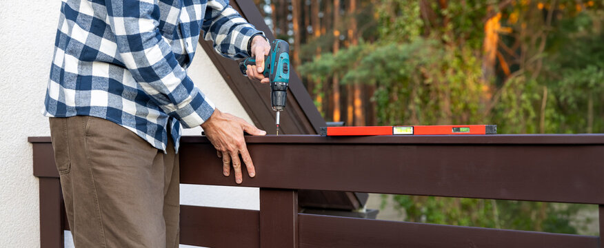 Worker installing wooden balcony railing with screwdriver during house construction