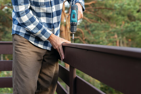 Worker installing wooden patio railing with screwdriver during house construction