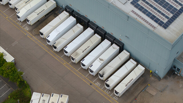 Aerial view of an industrial warehouse with multiple semi-trucks parked at loading bays, featuring solar panels on the roof and marked parking spaces in Birmingham, England, United Kingdom.