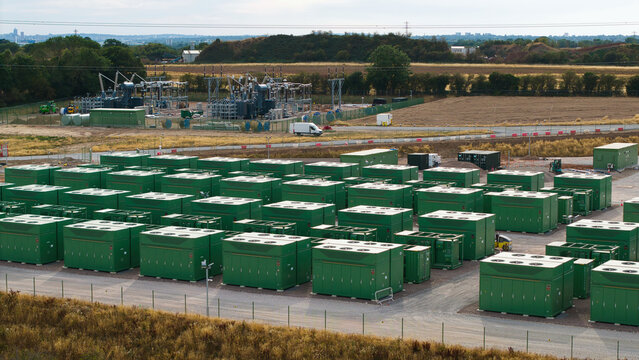 Aerial view of Battery Energy Storage Systems with rows of green battery containers and an electrical substation in the background in Birmingham, England, United Kingdom.