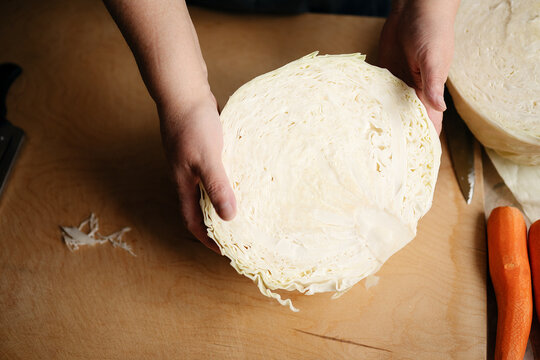 Fresh white cabbage cut in half and handled on a wooden kitchen worktop during vegetable preparation for homemade cooking.
