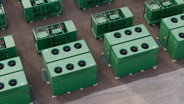 Aerial view of green containerized battery energy storage systems with cooling fans arranged on a gravel site in Birmingham, England, United Kingdom.
