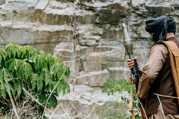 Naklejka premium Serious outdoor soldiers in jungle on duty holding rocket launcher weapon with vigilant expression near rocky cliff face wall