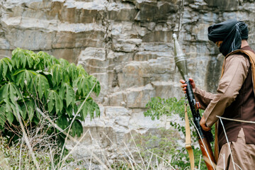 Naklejka premium Militant fighter holding weapon rocket launcher dangerous serious expression outdoor rocky mountain environment prepared for conflict