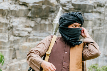 Naklejka premium Armed fighter warrior with rocket launcher, determined expression, middle eastern man in traditional headwear, tactical military conflict zone