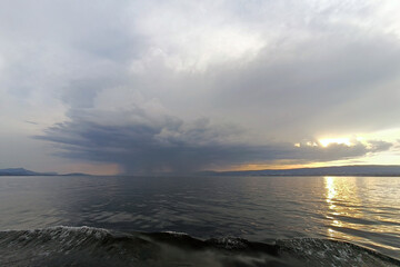 Fototapeta premium Dramatic Storm Clouds and Rain over Lake at Sunset with Golden Reflection on Water