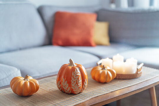 Cozy warm autumn home interior - decorative orange ceramic pumpkins, candles on the wooden coffee table and gray sofa with bright cushions on background . Scandinavian minimalist hygge home fall decor