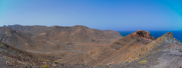 Obraz premium Panoramic view of arid volcanic mountains and coastal cliffs overlooking Atlantic Ocean in Fuerteventura, Canary Islands.