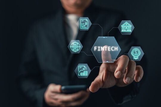 Businessman touching a glowing virtual fintech interface with financial icons. Mobile banking, digital transformation, cryptocurrency, and modern investment concept on dark background.