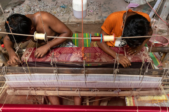 Narayanganj, Bangladesh - 29 August 2021: View of two weavers working on a traditional handloom to create an intricate Jamdani saree with colorful threads.