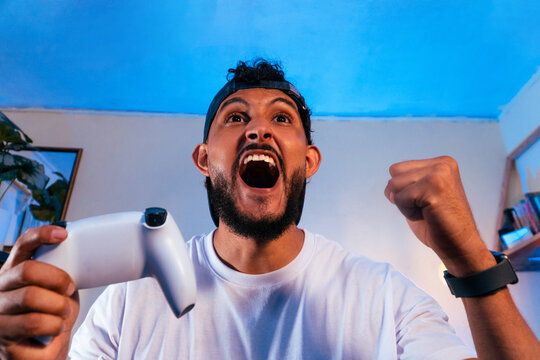 Hispanic adult gamer celebrating victory playing video game
