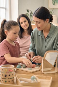 Woman speech therapist doing tactile sensory play with little girl while mother observing during home consultation.