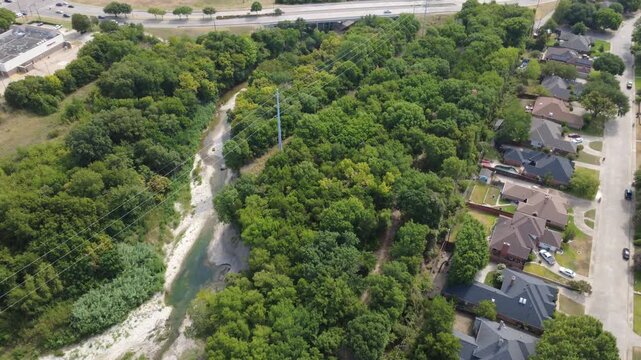 Exposed limestone riverbeds wind beside Mesa Verde subdivision in suburbs. Transmission pylons, thick woodland foliage, backyard rooftops highlight natural municipal corridors, DeSoto, TX