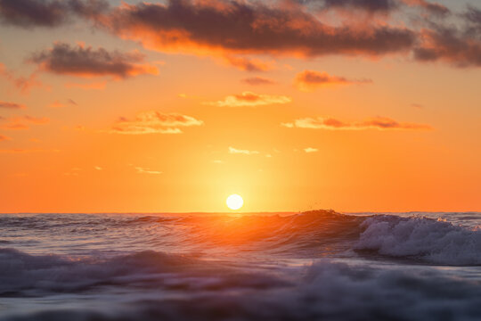 Bright setting sun over ocean waves during a fiery orange sunset
