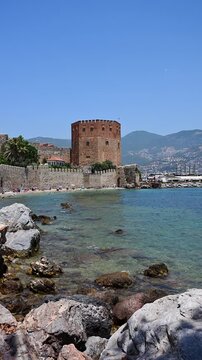 Historic Alanya Red Tower, castle walls from rocky beach, ancient Kizil Kule medieval fortress near Mediterranean sea in Turkey, scenic summer travel concept. Kizil Kule and ancient stone castle wall