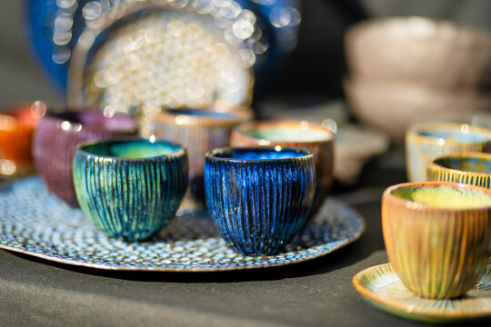 Handmade ceramic cups, bowls and vases displayed for sale at an outdoor craft market. Artisan pottery with unique glazes represents traditional craftsmanship and local small business.