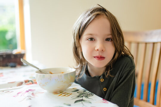 Young child sitting at a dining table and looking reluctant to eat his meal. Concept of picky eating, poor appetite and difficulties feeding children at home.